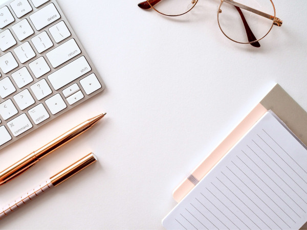 work desk with keyboard, pen, glasses, and notebook